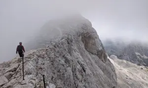 Turysta na skalistej ścieżce, wspinający się po via ferracie. Mgła otula szczyty, tworząc mistyczną atmosferę na szlakach Triglavu.