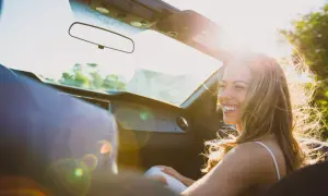 Vrolijke vrouw in cabriolet, haar haar wappert in de zon. Ze lacht, niet te streng voor jezelf, genietend van de rit.