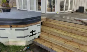 Pågår bygga badtunna. Isolerad stomme med trädetaljer och en grå presenning. Nya trätrappor leder upp till altanen.
