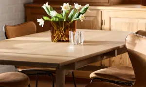 Ett ljust träbord med klassiska designstolar i läder. En vas med vita blommor och glas står på bordet.