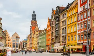 Bunte Häuserfronten am Wroclaw Rynek, mit einem markanten Turm im Hintergrund. Menschen spazieren über den gepflasterten Platz.