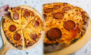 En hand tar en bit av en klassisk neapel pizza med pepperoni och smält ost.