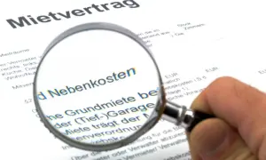 Lupe auf Mietvertrag, um Nebenkosten zu prüfen. So können Sie Ihre Warmmiete berechnen.