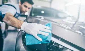 Mężczyzna w białych rękawiczkach czyści błyszczącą karoserię samochodu niebieską mikrofibrą. Używa do tego uniwersalnego środka czyszczącego, czyli APC zasadowego, aby usunąć wszelkie zabrudzenia.