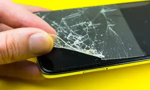 Dłoń zdejmuje pęknięte szkło hartowane 9h z ekranu telefonu.