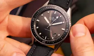 Manos ajustando un reloj automático Blancpain Fifty Fathoms Bathyscaphe con correa de tela negra.