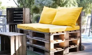 Kanapa z palet i skrzynek, ozdobiona żółtymi poduszkami. To przykład, upcycling co to znaczy: nadawanie drugiego życia przedmiotom.