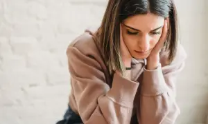 Een jonge vrouw met haar handen tegen haar slapen, diep in gedachten verzonken. Ze lijkt te worstelen met de gevolgen van gaslighting door vrouwen, haar blik neergeslagen.