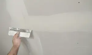 Hand verspachtelt Rigipsplatten mit einem Spachtel. Die Naht wird geglättet, um eine ebene Oberfläche für die weitere Bearbeitung zu schaffen.