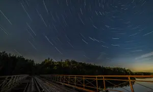 Nocne niebo nad starym mostem, gdzie gwiazdy kreślą na ciemnym tle świetliste ślady.