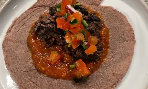 En lila tortilla med en klick refried beans, toppad med salsa och hackad lök.