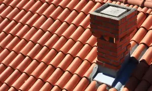 Ceglany komin na dachu z dachówki. Dowiedz się, jak uszczelnić komin w mieszkaniu, by uniknąć przecieków.