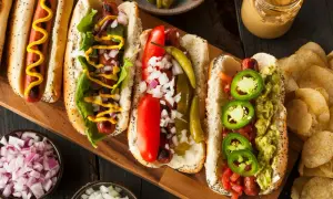 Cztery pyszne hot dogi z różnymi dodatkami: musztarda, cebula, pomidor, papryczki i guacamole.