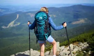Kobieta z turkusowym plecakiem w góry, z kijkami trekkingowymi, podziwia panoramę. Idealny plecak na górskie wędrówki.