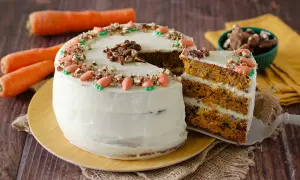 Torta di carote con glassa bianca, decorata con carote di zucchero e noci. Una fetta mostra gli strati soffici, perfetta per una carrot cake ricetta semplice.