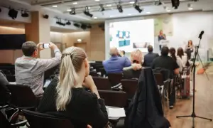 Uczestnicy konferencji, gdzie odbywają się **usługi szkoleniowe**. Jedna osoba filmuje prezentację telefonem.