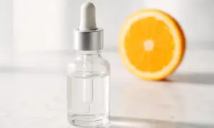 Siero con vitamina C per combattere le macchie della pelle, accanto a una fetta d'arancia.