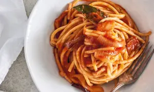 En skål med bucatini all'amatriciana, en klassisk italiensk pastarätt med tomatsås, lök och en lagerblad.