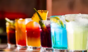 Kolorowe drinki na barze, w tym niebieski koktajl z plasterkiem cytryny, przypominają letnie orzeźwienie, jak Bacardi Razz drink.
