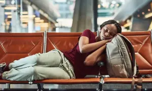 Frau schläft auf einer Bank im Flughafen bei Nacht, ihr Kopf ruht auf ihrem Rucksack.