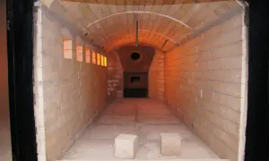 Wnętrze krematorium z ceglanymi ścianami i łukowym sufitem, oświetlone pomarańczowym blaskiem.