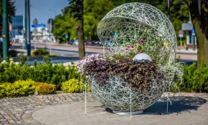 Ozdobna kula z kwiatami, przykład instalacji artystycznej. Wplecione w ażurową konstrukcję rośliny tworzą efektowną kompozycję.