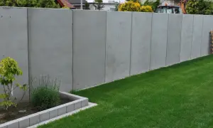 Nowy, wysoki betonowy płot dzieli działki, symbolizując konflikt z sąsiadem o ogrodzenie.