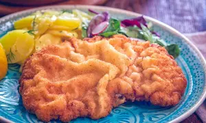 Ein knuspriges Wiener Schnitzel mit Kartoffelsalat und Zitrone auf einem blauen Teller.