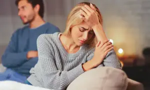 Una mujer angustiada en primer plano, con un hombre de espaldas en el fondo. La escena evoca la confusión y el dolor que a veces acompañan a **que es la limerencia**.