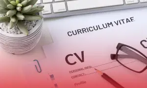 Na biurku leżą dokumenty CV, okulary i ołówek. Roślina w doniczce i klawiatura dopełniają scenę.