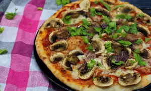 Pyszna pizza z pieczarkami na pizze, cebulą i świeżą natką pietruszki, podana na kraciastej serwetce.