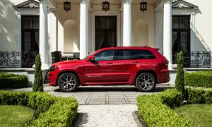 Czerwony Jeep Grand Cherokee SRT zaparkowany przed elegancką posiadłością z białymi kolumnami i zadbanym ogrodem.