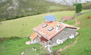 Refugio en Picos de Europa, con paneles solares en el tejado. Vacas pastan en la ladera verde.