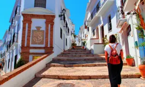 Una mujer con mochila sube escaleras empedradas en un pintoresco pueblo blanco, quizás el pueblo mas bonito de Andalucia.
