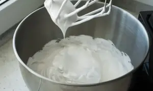 Ubita śmietana z mascarpone, puszysta i idealna do deserów, właśnie powstaje w metalowej misie miksera.