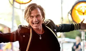 Petter Stordalen, trots sin ålder, strålar av energi i en mörk jacka med gulddetaljer. Han ler brett och gestikulerar.