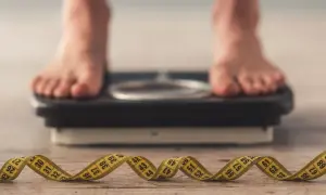 Pieds sur une balance, ruban à mesurer enroulé au premier plan. La question "pourquoi je ne perds pas de poids" résonne.