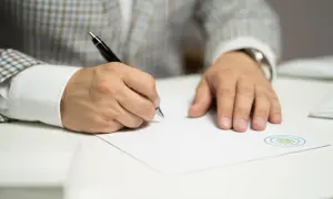 Mężczyzna w eleganckim garniturze podpisuje dokument. To ważny wniosek o stwierdzenie nabycia spadku, który wymaga precyzji i uwagi.