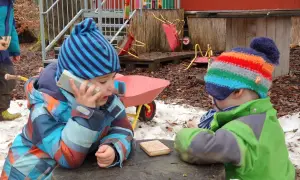 Zwei Kinder im Wald Kindergarten spielen mit einem Spielzeugtelefon und einem Holzklotz.