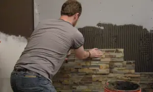 Mężczyzna układa kamień dekoracyjny betonowy. Do cięcia takiego materiału używa się specjalistycznych narzędzi.