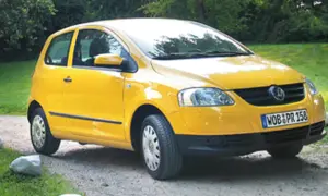 Żółty Volkswagen Fox zaparkowany na żwirowej drodze, otoczony zielenią.