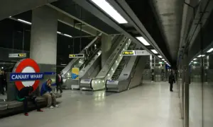 Stacja Canary Wharf w **metro londyn** z charakterystycznym znakiem, ruchomymi schodami i ludźmi czekającymi na pociąg.
