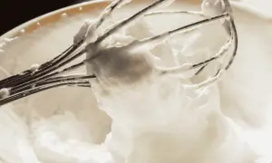 Un batteur électrique en train de battre les blancs en neige dans un bol. La mousse est aérienne et forme des pics.