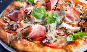Pyszna pizza parma z szynką, pieczarkami, pomidorami i bazylią, posypana parmezanem.