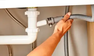 Ręka dokręca obejmę, łącząc wąż odpływowy ze zlewem.