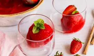 Erfrischendes Erdbeer Sorbet in Gläsern, garniert mit Minze. Daneben frische Erdbeeren und eine Schüssel mit dem leuchtend roten Sorbet.