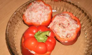 Trzy czerwone papryki faszerowane surowym mięsem mielonym i ryżem, gotowe do pieczenia.
