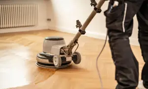 Ein Handwerker versiegelt einen Parkettboden mit einer Poliermaschine. Der frisch versiegelte Boden glänzt.