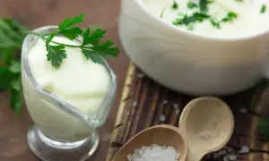 Cremige Bechamel-Sauce in einer Sauciere, garniert mit Petersilie. Daneben eine Schüssel mit der Sauce und grobes Salz auf Holzlöffeln.