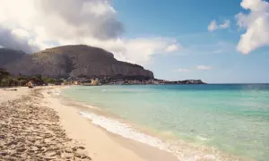 Piękna plaża Mondello z turkusową wodą, piaszczystym brzegiem i malowniczym miasteczkiem u podnóża góry.